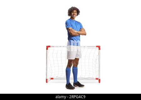 Full length portrait of an african american football player in a blue jersey posing with folded arms in front of a mini goal isolated on white backgro Stock Photo