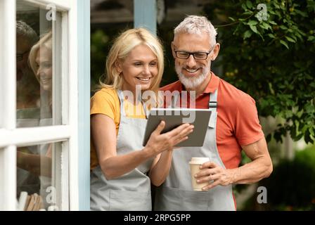 Happy mature couple drinking coffee and using digital tablet outdoors Stock Photo
