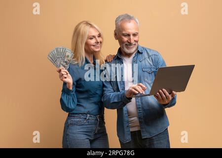 Happy elderly couple spouses using computer laptop, holding cash Stock Photo