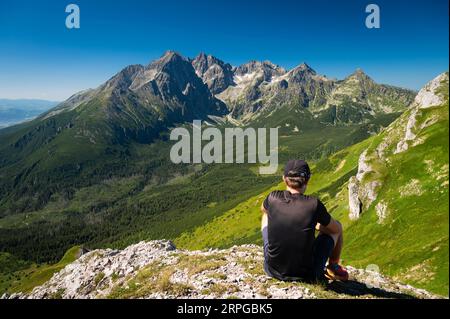 Embracing the beauty of the Belianske Tatras, a young traveler revels in serenity, all while the High Tatras' grandeur unfolds in the backdrop. Stock Photo