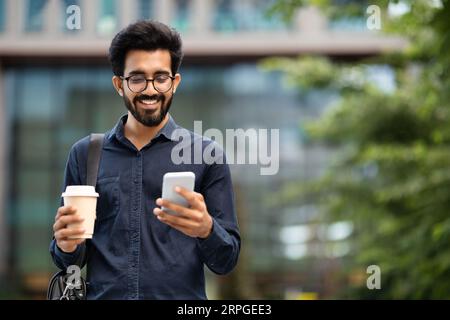 Positive indian guy employee going to office, drinking coffee Stock Photo