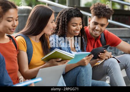 Diverse Multiethnic Students Reading Books And Using Digital Tablet Outdoors Stock Photo