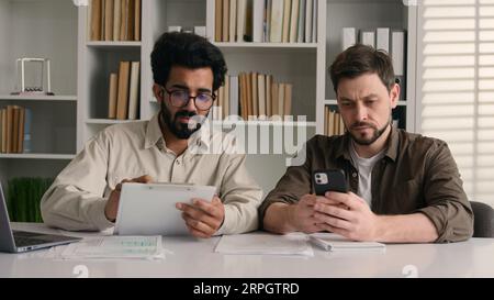 Two businessmen multiracial men co-workers in office Arabian Indian businessman show papers business project on laptop to colleague Caucasian man Stock Photo