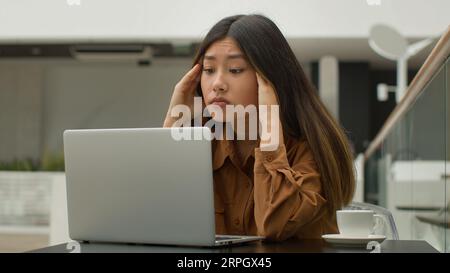 Exhausted overworked Asian chinese japanese woman student girl studying online with laptop in cafe tired sick businesswoman think difficult decision Stock Photo