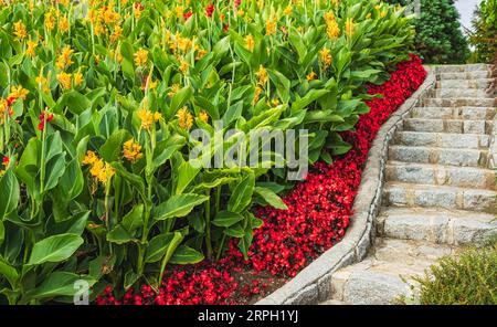 Curving stone stairway with surrounding beautiful flowers. Stairway in a summer garden. Staircase lined with flowers and plants in public park. Stone Stock Photo
