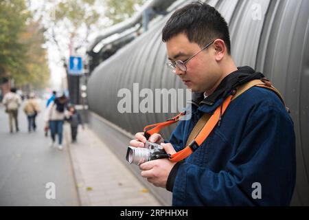 191109 -- BEIJING, Nov. 9, 2019 -- Liu Gaochao checks camera settings as he goes for some shots at the 798 art zone in Beijing, capital of China, Nov. 9, 2019. It s been more than five years since Liu Gaochao embraced a career in film developing. On top of a high-rise mansion next to Liufang Station of Beijing Subway Line 13, Liu runs a studio, New Wave Film Lab, which also provides him a place to live. In 2012, Liu left his hometown in central China s Henan Province and headed for Beijing in pursuit of better opportunities. After he settled down in the capital city, he came across film photog Stock Photo