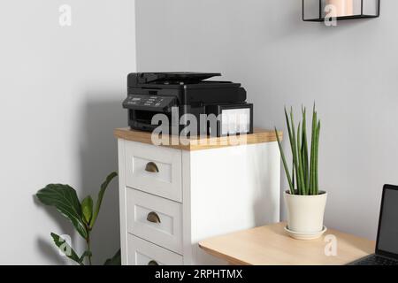 Modern printer on chest of drawers near wooden table indoors Stock Photo