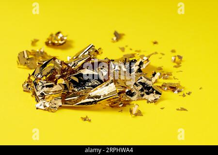 Many pieces of edible gold leaf on yellow background Stock Photo