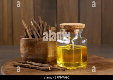 Dried sticks of licorice roots and essential oil on wooden board, closeup Stock Photo