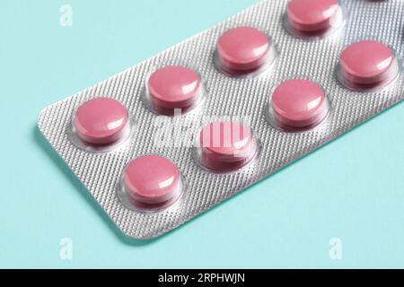 Pink pills in blister on turquoise background, closeup Stock Photo