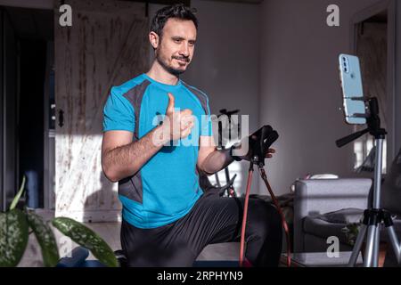 Attractive latin man personal trainer recording with phone content for online fitness business. Freelance filming online training program with virtual Stock Photo