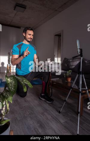 Filming online classes with confident professional fitness trainer. Exercising at home. Young sports man blogger recording video on phone camera. Stock Photo