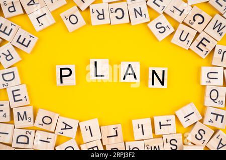 The PLAN word on wooden cubes. Alphabet blocks with heap of letters on yellow background. Stock Photo