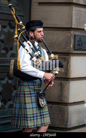 man playing the bagpipes dressed in traditional Scotish clothing on the Royal Mile in Edinburgh Scotland Stock Photo
