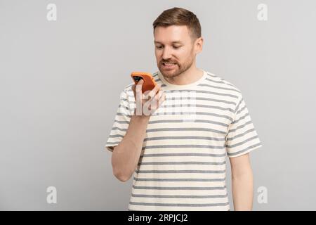 Puzzled man receiving sms reading frustrating message in smartphone on grey background.  Stock Photo