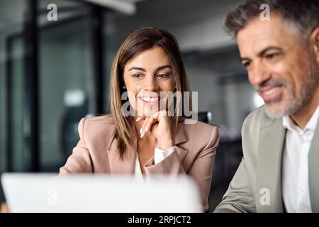 Smiling business woman working on laptop with male colleague at office meeting. Stock Photo