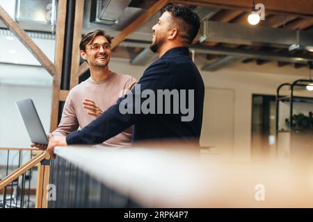 Male tech professionals having a discussion in an office. Two business men talking about a project while standing on an interior balcony. Stock Photo
