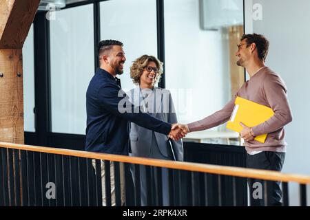 Successful business men shaking hands over a promotion in an office. Happy business professionals reaching an agreement on an internal recruitment dea Stock Photo