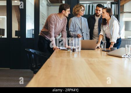 Design team discussing a project in a meeting, they're standing together around a laptop in a boardroom. Group of business professionals talking about Stock Photo
