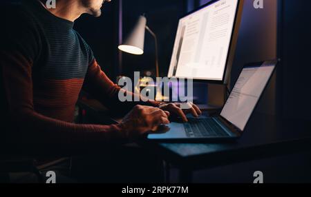 A caucasian male entrepreneur works late from his home office, focused on a business project. He types on his laptop, dedicated to meeting a deadline. Stock Photo