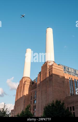 Battersea, London, England - 29th July 2023: A Qatar Airways plane flies past the iconic chimneys of Battersea Power Station in London against a blue Stock Photo