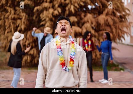 Happy man with flower necklace laughing while having a party with friends outdoors. Party and celebration concept. Stock Photo