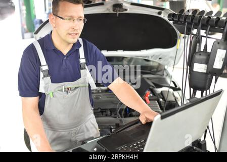 car mechanic maintains a vehicle with the help of a diagnostic computer - modern technology in the car repair shop Stock Photo