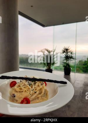 A carbonara spaghettis with a beautiful landscape view in the background served in a white plate. Stock Photo