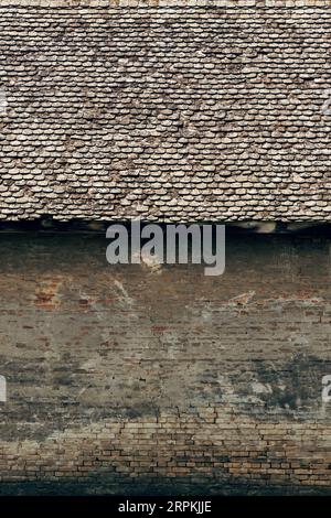 Old abandoned house with damaged brick wall and worn roof tiles as background Stock Photo