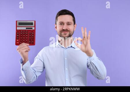 Happy accountant with calculator showing ok gesture on violet background Stock Photo