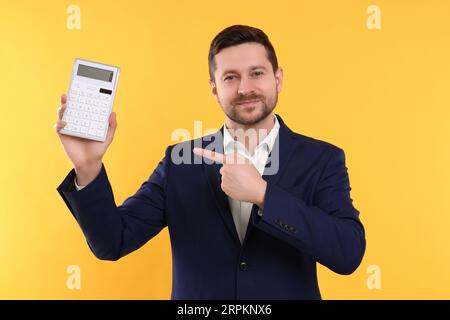 Happy accountant showing calculator on yellow background Stock Photo