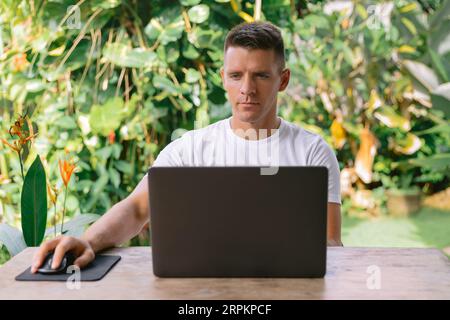 Focused young man using laptop, successful freelancer working online on computer sitting in modern kitchen Stock Photo