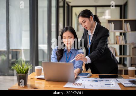 A professional and confident Asian businesswoman or female manager in a formal black suit is helping her colleague on a project, sharing her ideas, gi Stock Photo
