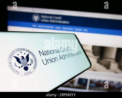Mobile phong with seal of National Credit Union Administration (NCUA) on screen in front of website. Focus on center-left of phone display. Stock Photo