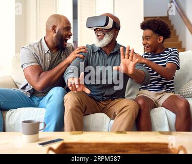 Grandfather Wearing VR Headset As Multi-Generation Male Family Sit On Sofa At Home Together Stock Photo