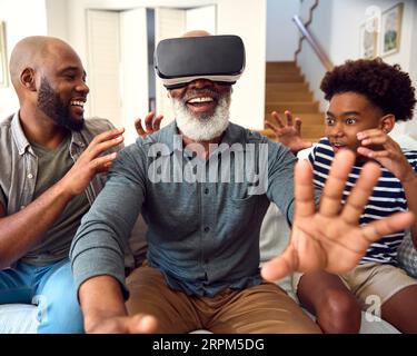 Grandfather Wearing VR Headset As Multi-Generation Male Family Sit On Sofa At Home Together Stock Photo