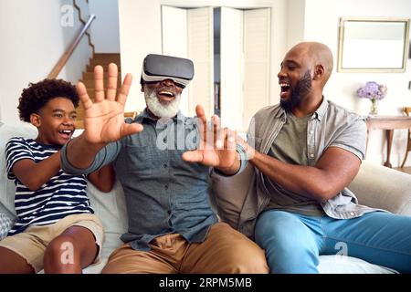 Grandfather Wearing VR Headset As Multi-Generation Male Family Sit On Sofa At Home Together Stock Photo