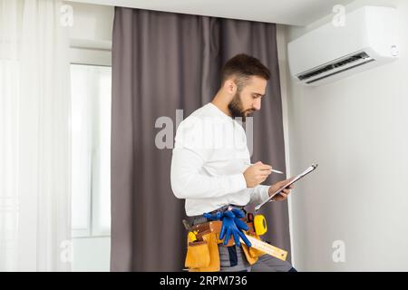 male technician service worker diagnosing for repairs air conditioner. person using tablet. Stock Photo