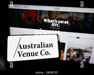 Person holding cellphone with logo of company Australian Venue Co. (AVC) on screen in front of business webpage. Focus on phone display. Stock Photo