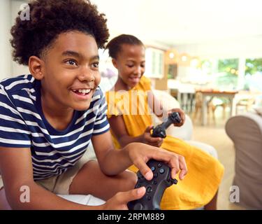 Brother And Sister Sitting On Sofa At Home Playing Video Game Together Stock Photo