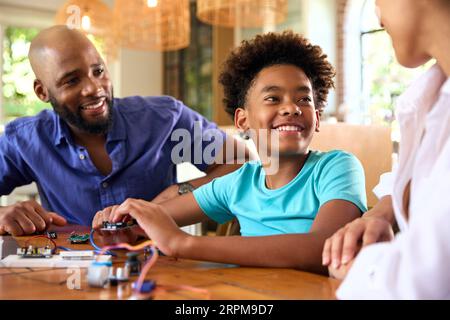 Family Around Table At Home Using Laptop With Parents Helping Son With Science Homework Stock Photo