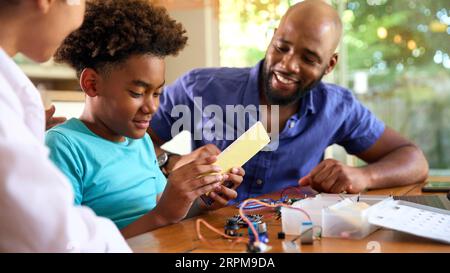 Family Around Table At Home Using Laptop With Parents Helping Son With Science Homework Stock Photo
