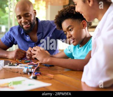 Family Around Table At Home Using Laptop With Parents Helping Son With Science Homework Stock Photo