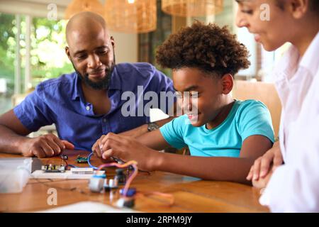 Family Around Table At Home Using Laptop With Parents Helping Son With Science Homework Stock Photo