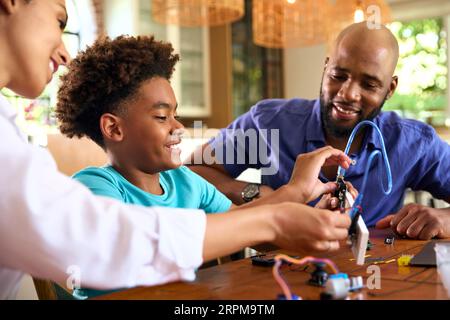 Family Around Table At Home Using Laptop With Parents Helping Son With Science Homework Stock Photo