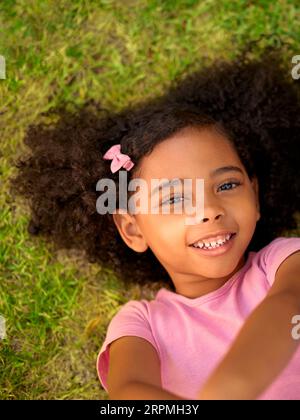 POV Overhead Shot Of Smiling Girl Lying On Grass Taking Selfie On Mobile Phone Stock Photo