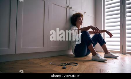 Demotivated Nurse Wearing Uniform Sitting On Floor At Home After Long Shift Stock Photo