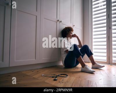 Demotivated Nurse Wearing Uniform Sitting On Floor At Home After Long Shift Stock Photo