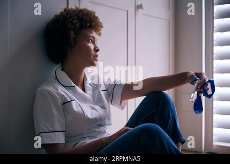 Demotivated Nurse Wearing Uniform Sitting On Floor At Home After Long Shift Stock Photo