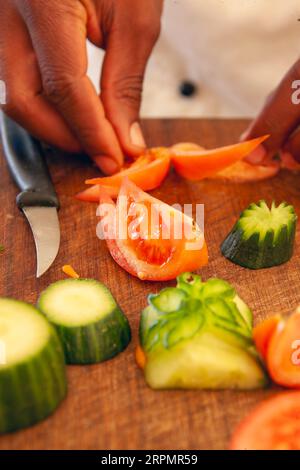 african american chef cutting  and garnishing cucumbers and tomatoes for a vegetarian meal on a wooden chopping board Stock Photo